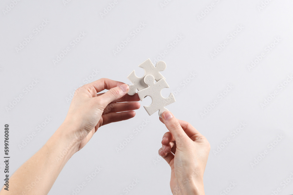 Woman's hands hold puzzle pieces on gray background. Business concept, teamwork Woman's hands hold puzzle pieces on gray background. Business concept, teamwork