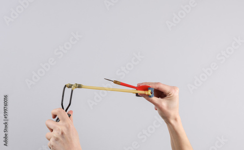 Hands holding slingshot with darts on gray background. Business concept