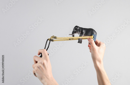 Hands holding slingshot with toy elephant on gray background.