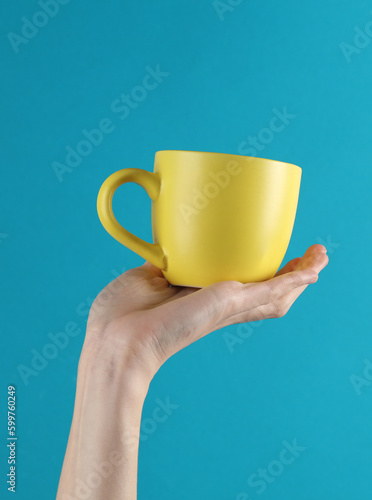 Woman's hand holds a yellow ceramic cup on a blue background