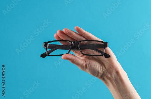 Female hand hold eyeglasses on a blue background. Eye examination, ophthalmologist