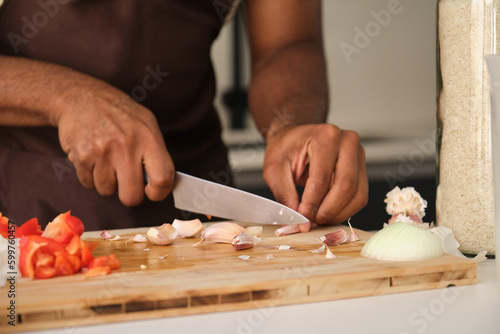 Unrecognizable young african man peeling garlic in a kitchen.
