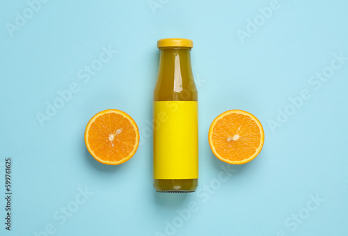 Bottle of orange juice with half a juicy orange on blue background. Top view