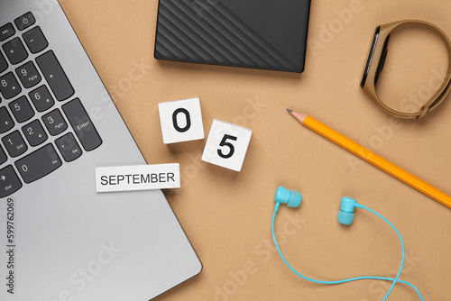 White wooden block calendar with date september 05 and modern gadgets, school or student accessories on beige background. Top view