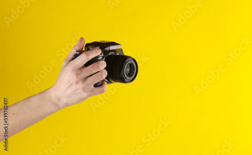Woman's hand holding a modern digital camera on a yellow background