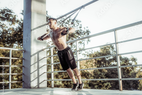 Young muscular male athlete exercising with resistance outdoors. Functional training.