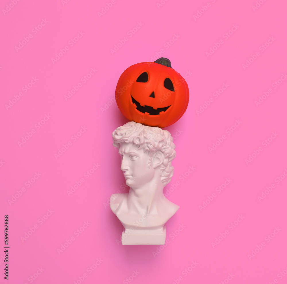 Plaster bust of David with jack lantern pumpkin head on pink background. Halloween concept. Minimal still life photo Plaster bust of David with jack lantern pumpkin head on pink background. Halloween concept. Minimal still life photo