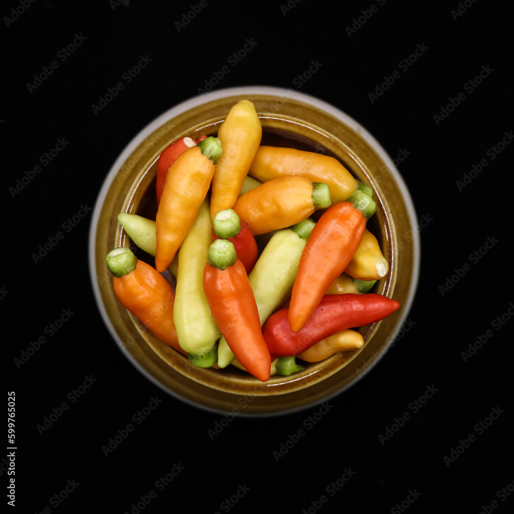 closeup shot of fresh organic hot chili peppers in red, orange and yellow colors stored in a traditional pot jar isolated in a black background closeup shot of fresh organic hot chili peppers in red, orange and yellow colors stored in a traditional pot jar isolated in a black background