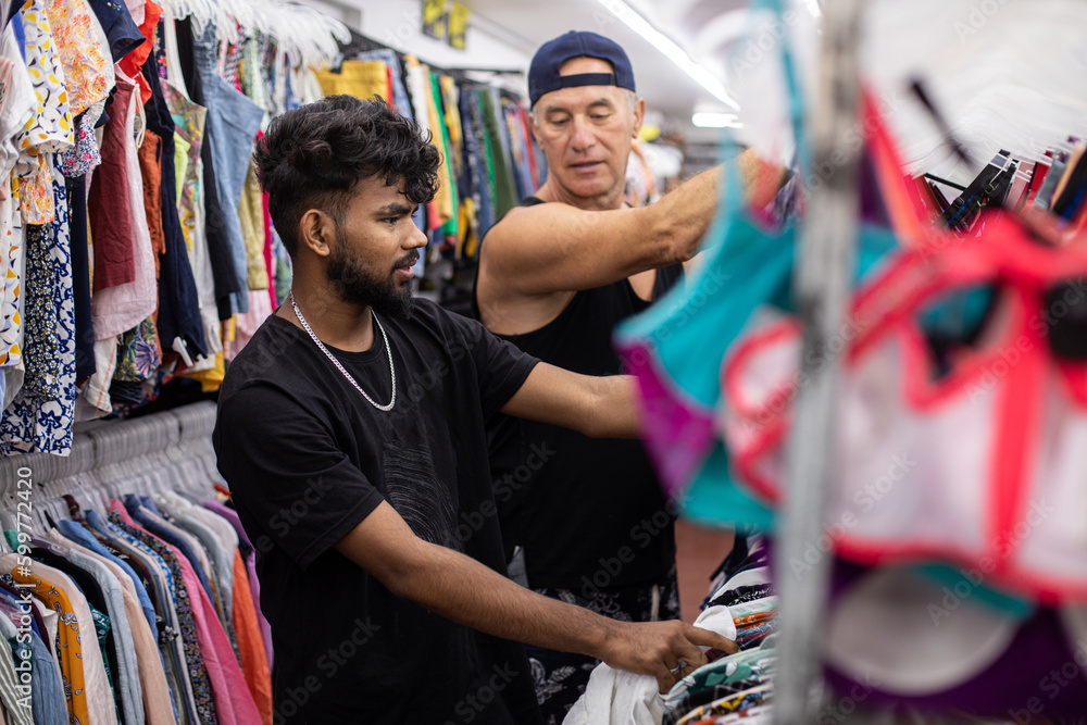 Portrait of customers in black t-shirts peeping and selecting cheap clothes for casual life inside shop center 
