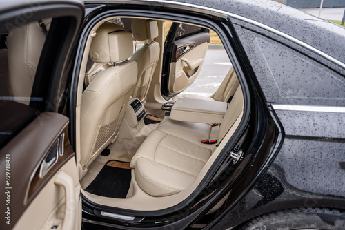 Exterior of black modern car and interior of new expensive car. Open passenger door rear left, right. Leather clean interior design, car driver seats, buttons, dashboard, nappa leather, beige. Closeup © Serhii