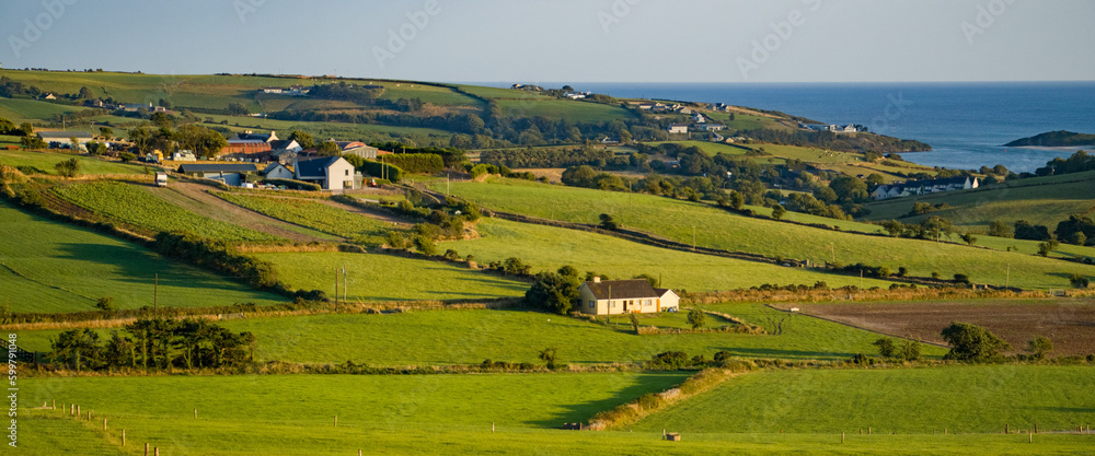 farm fields in the Ireland on a summer evening. Agricultural Irish landscape. Pastures for livestock, house on green grass field.