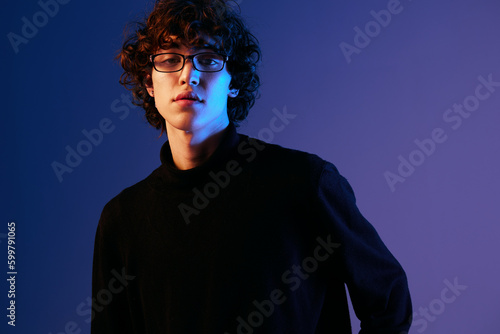 Male fashion portrait in black clothes model poses in glasses, hipster lifestyle, portrait blue background, mixed neon light, fashion style and trends boys teenager, copy space