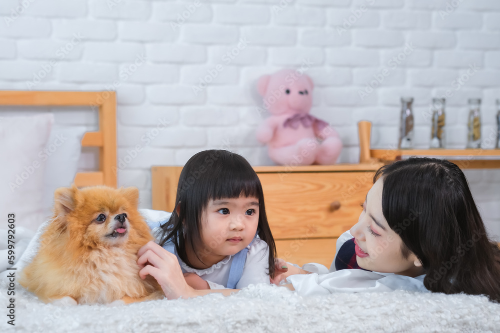 Beautiful asian girl and little girl lying on bed with the dog with pure joy and delight on their faces both sharing the happiness that the furry friend brought to them. Beautiful asian girl and little girl lying on bed with the dog with pure joy and delight on their faces both sharing the happiness that the furry friend brought to them.