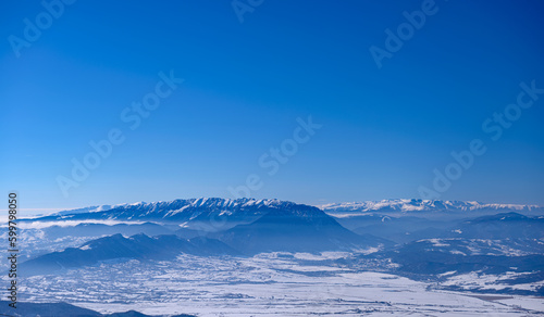 Incredible winter landscape of alpine valley under bright sunny light in frosty morning, beautiful alpine panoramic view of snow capped Piatra Craiului and Fagaras mountains in background, Romania © Creatikon Studio