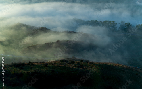 Aerial view of the valley in early morning mist, beautiful in the highlands. Low clouds and fog cover the sleeping meadow. Alpine mountain valley mists landscape at dawn. Serene moment in rural area