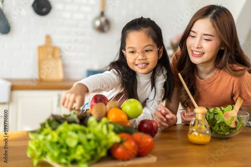 Portrait of enjoy happy love asian family mother with little asian girl daughter child having fun help cooking food healthy, strong, eat together with fresh vegetable salad ingredient in kitchen