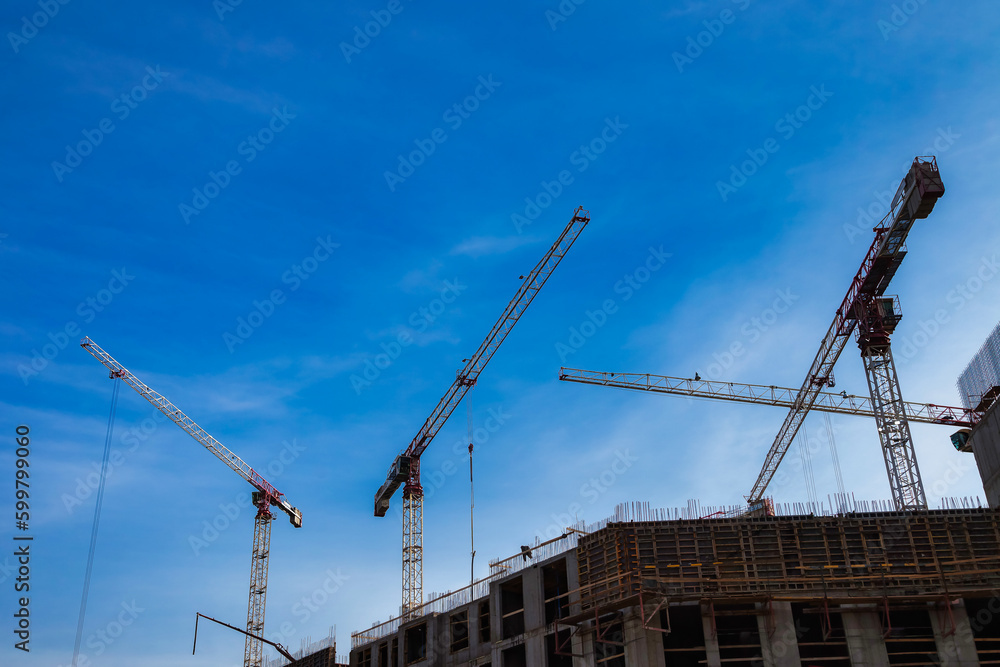 Backdrop of industrial cranes on construction site house building at blue sky. Industry crane on creation site. Construction and renovation of buildings concept. Copy advertising text space, banner