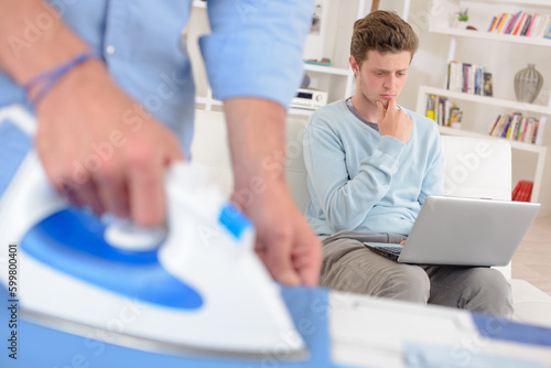 Man ironing, teenager using laptop looking concerned