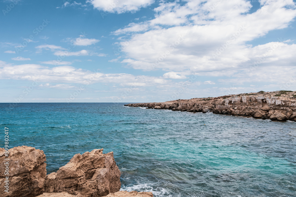 Turquoise blue sea and rocky coast, blue lagoon in Cyprus. Landscape with blue sea water, rocks and blue cloudy sky in the background