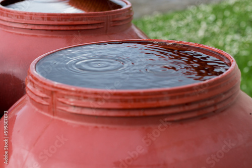 Rain is falling into a red barrel filled with water in the garden. Rainwater collection for irrigation. No waste of water. Drought problem in 2023.