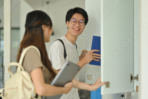Two young college friends talking while standing at lockers in campus hallway. Education  Learning and technology concept
