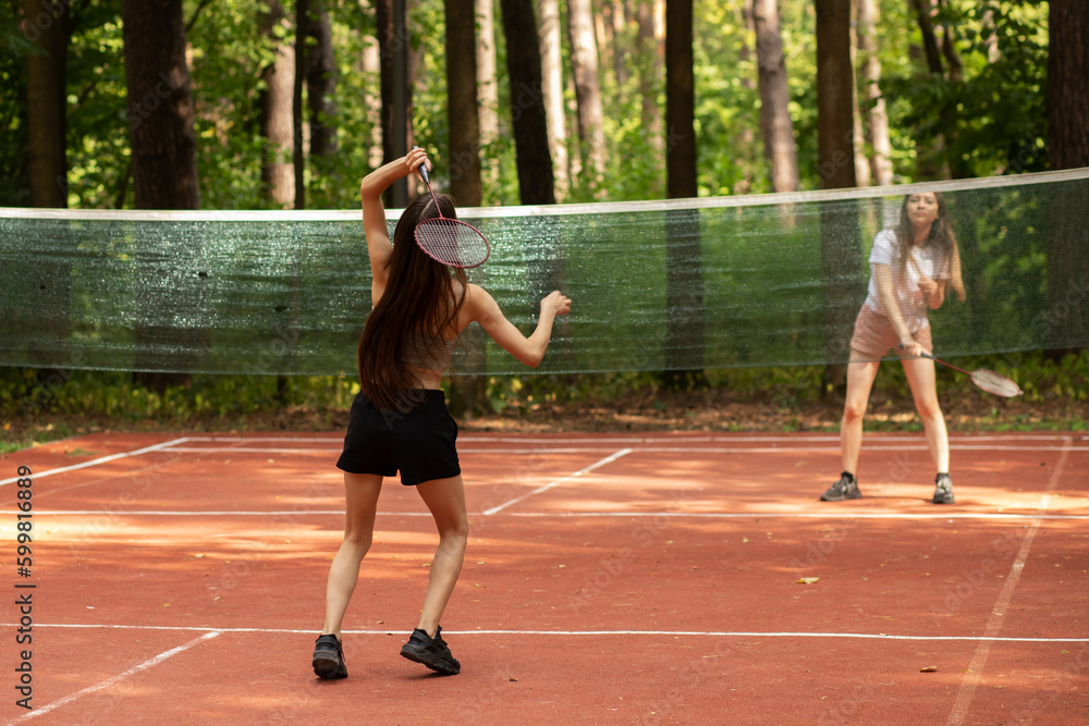 teenager sport outdoor, two girls play badminton in the park in nature on a sunny summer day, badminton competition