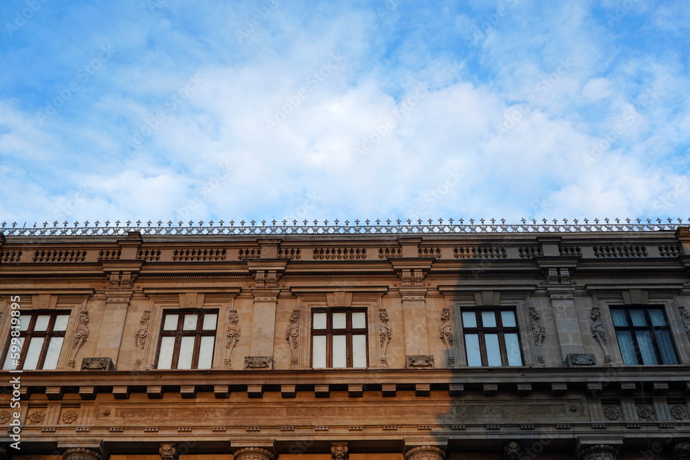Top floor of historical building in neoclassical architecture style with row of architrave windows with molded lions, balustrade and dentil decorations Top floor of historical building in neoclassical architecture style with row of architrave windows with molded lions, balustrade and dentil decorations