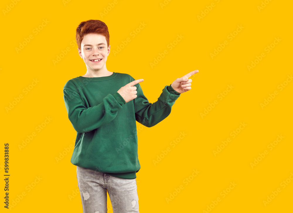 Cheerful teen boy pointing aside at empty space yellow background. Portrait of handsome emotional redhead boy in green sweatshirt pointing index fingers up. Advertising concept Cheerful teen boy pointing aside at empty space yellow background. Portrait of handsome emotional redhead boy in green sweatshirt pointing index fingers up. Advertising concept