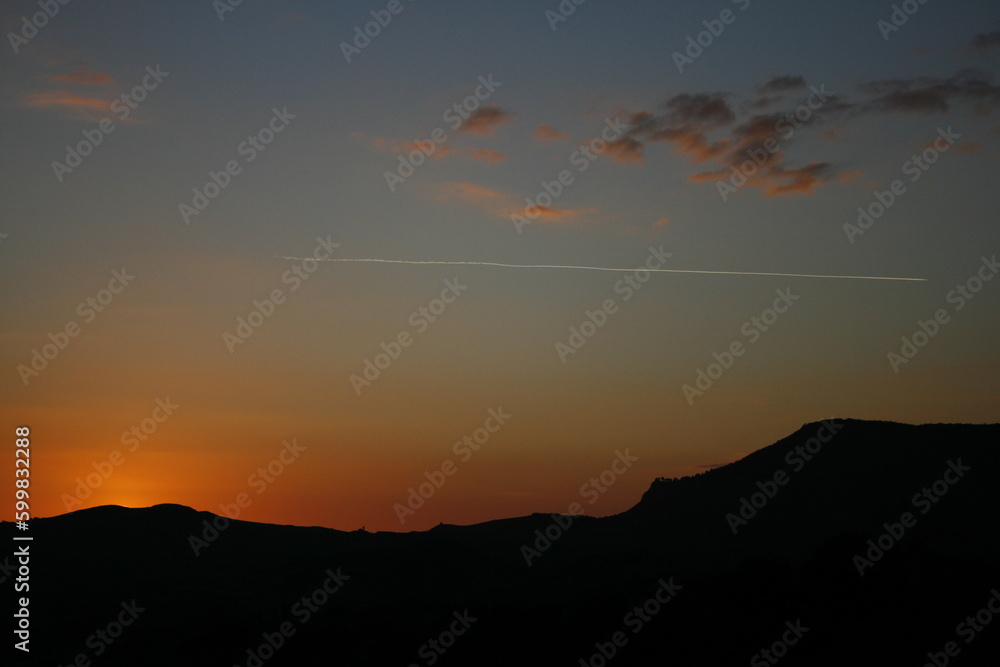 Rural scene at sunset, sparse clouds and airplane trail 