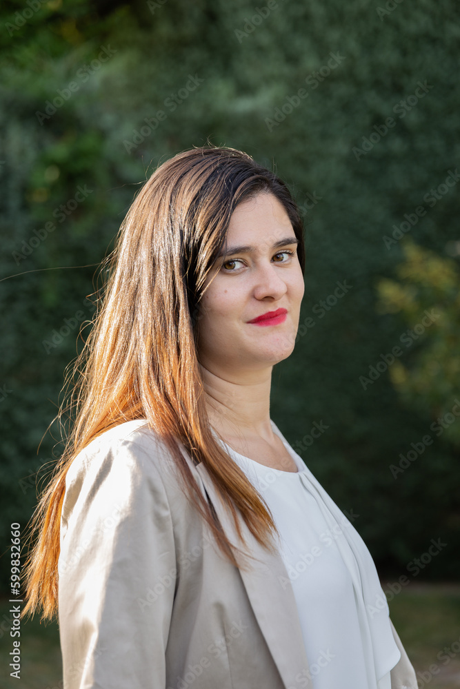 Portrait of young Caucasian woman with red lips and long brown hair, smiling and calm in a sunny garden at sunset with relaxed and calm attitude Portrait of young Caucasian woman with red lips and long brown hair, smiling and calm in a sunny garden at sunset with relaxed and calm attitude