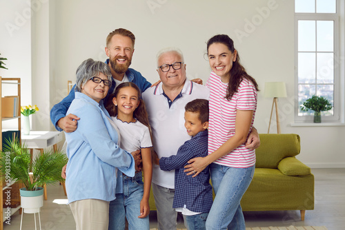 Portrait of a happy beautiful extended multi generational family all together at home. Cheerful, joyful children, parents and grandparents standing in the living room, hugging and smiling