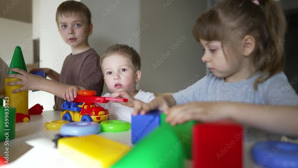 Happy family. Puzzle game. Colored toy in the hands of children. Teaching children in kindergarten. Boys and girls teamwork build cubes. Colored blocks and toy car on table in kindergarten. Schooling Happy family. Puzzle game. Colored toy in the hands of children. Teaching children in kindergarten. Boys and girls teamwork build cubes. Colored blocks and toy car on table in kindergarten. Schooling