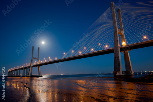Fototapeta Naklejka Na Ścianę i Meble -  The Vasco da Gama Bridge in Lisbon, Portugal at night with moon. Cable-stayed bridge. Tagus river. Horizontal shot. Long exposure.