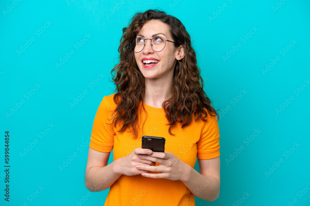 Young caucasian woman isolated on blue background using mobile phone and looking up Young caucasian woman isolated on blue background using mobile phone and looking up