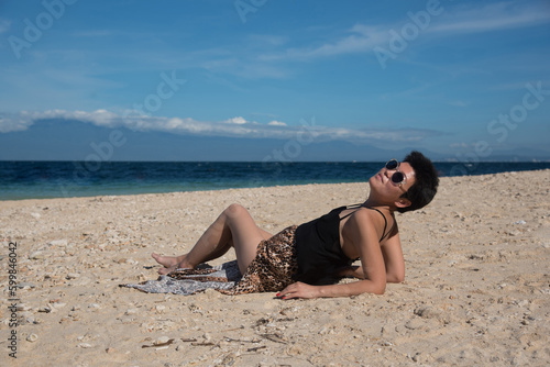 Asian girl lying at the beach in summer vacation. Stylish pretty woman with short black hair and leopart skirt. Copy space and blue sky on the background. Beauty lady with sunglasses.