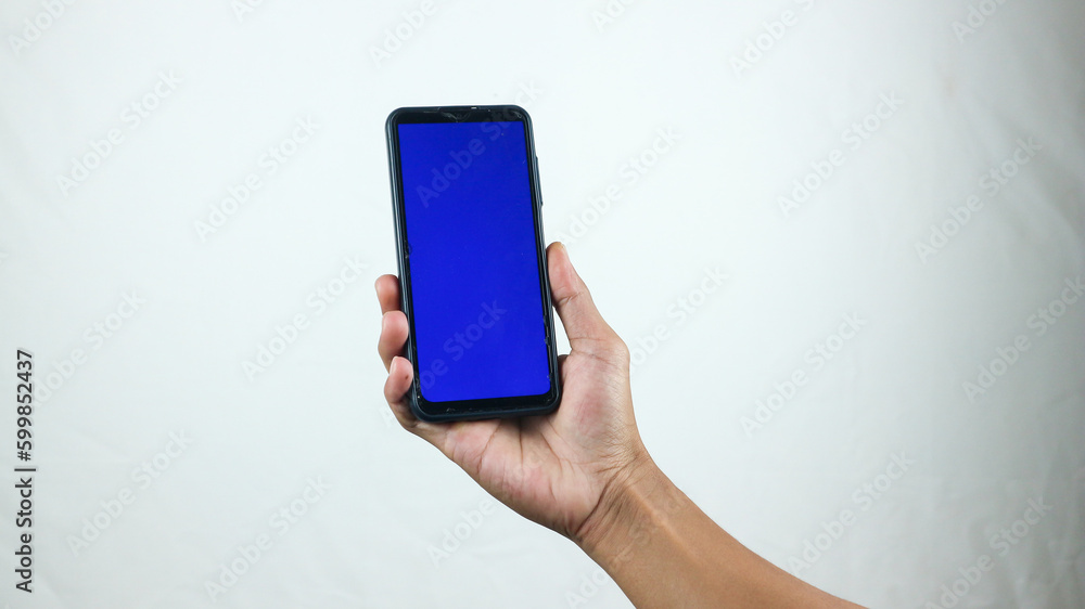 Asian man holding big smartphone with white, red, green, blue blank screen in hand, showing close to camera and pointing at device. Gadget with empty free space for mock up, banner