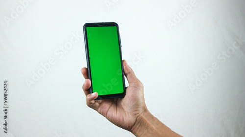 Asian man holding big smartphone with white, red, green, blue blank screen in hand, showing close to camera and pointing at device. Gadget with empty free space for mock up, banner