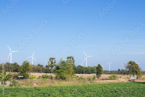 A wind turbine used to generate electricity is located on a green field on a blue sky background.