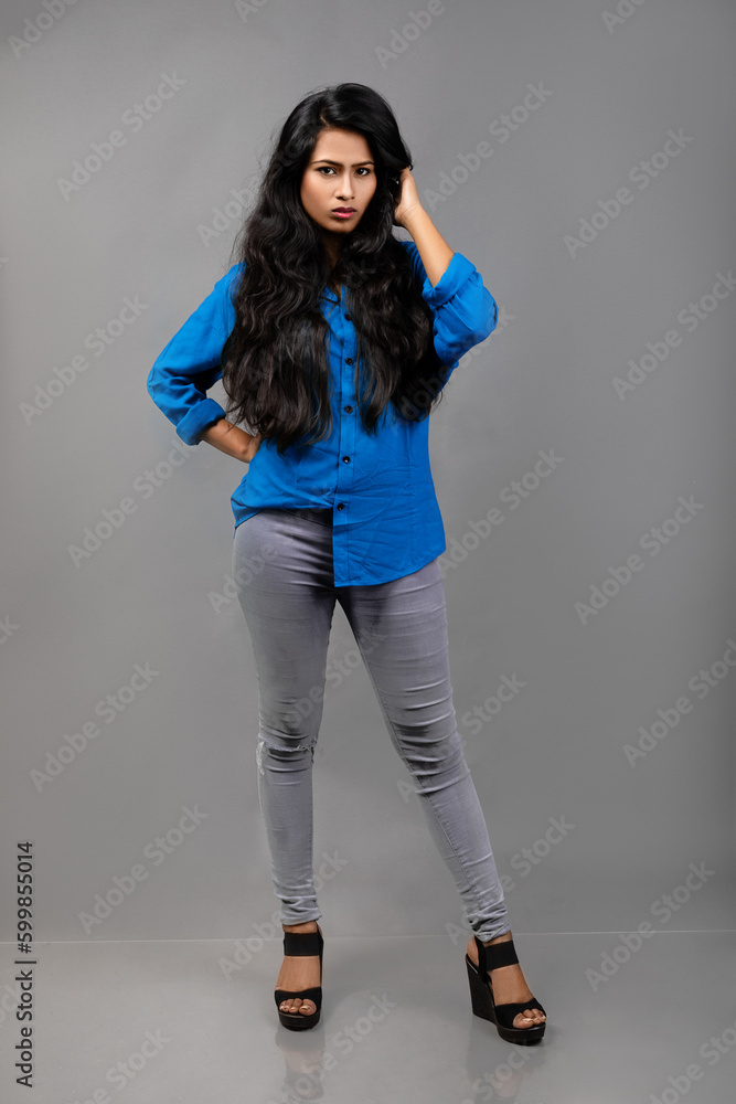 Indian female young model in casual wear against grey background - stock photo. Long black hair model wearing blue shirt. Indian female young model in casual wear against grey background - stock photo. Long black hair model wearing blue shirt.