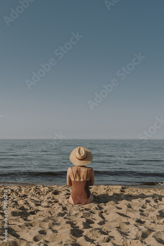 Pretty woman sitting on beach sand and watching at sea and sky. Minimal summer vacation concept. Chilling, relaxing near ocean inspirational composition