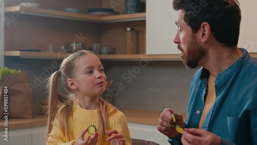 Caucasian father with little daughter at home kitchen cooking eating together child girl kid feed dad with cucumber slice daddy joking pretend feeding baby deceive cheat fooling around happy family