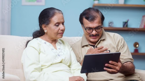 Indian senior couple talking with doctor on video call using digital tablet at home - concept of online consultation, medicare and home health care