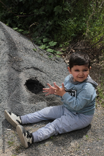 
the boy dug a hole in the sand, the child smiles and looks away