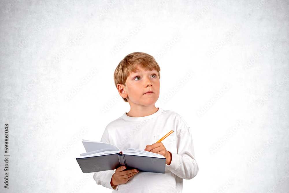 Inspired school boy taking notes, looking up on empty grey wall Inspired school boy taking notes, looking up on empty grey wall