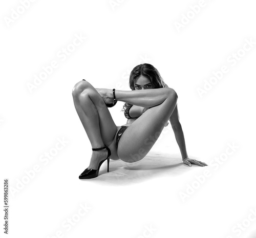 Beautiful flexible fitness woman with perfect legs sitting in an artistic pose in black lingerie and high heels black and white - fashion style on the studio background.