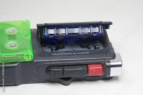 dictaphone for microcassettes. control keys block closeup. Blue cartridge with tape, inserted in lid of cassette compartment, green tape cassette laying on device