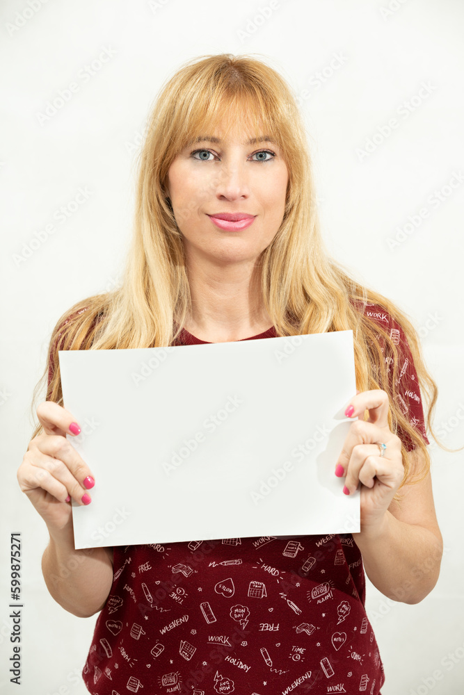 beautiful middle-aged blonde woman with light eyes and casual clothes holding a blank piece of paper at chest level in front of the camera with a completely white background. beautiful middle-aged blonde woman with light eyes and casual clothes holding a blank piece of paper at chest level in front of the camera with a completely white background.