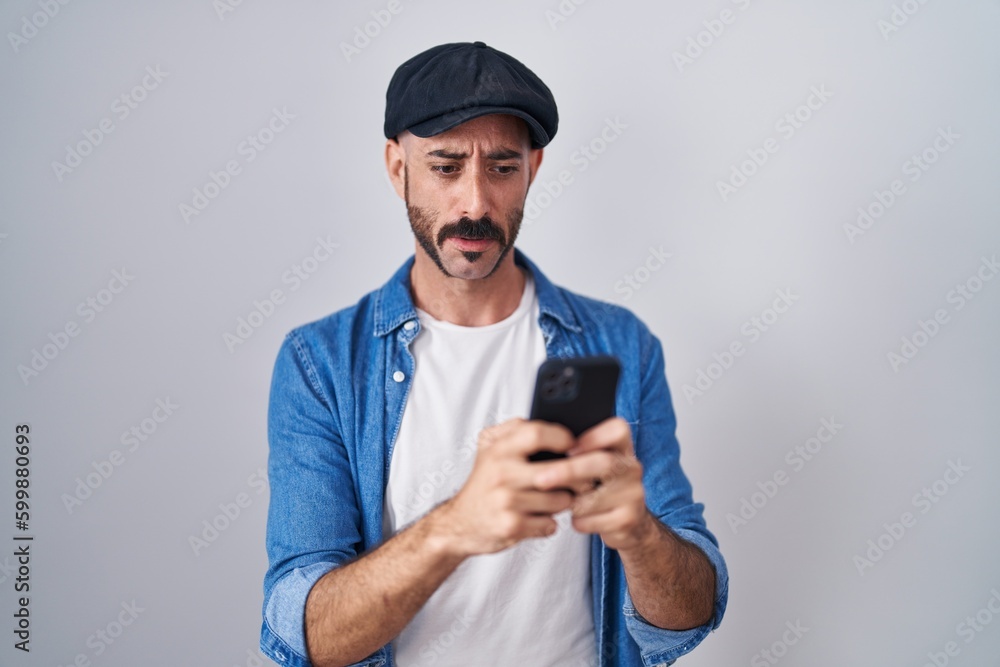 Hispanic man with beard using smartphone typing message clueless and confused expression. doubt concept. Hispanic man with beard using smartphone typing message clueless and confused expression. doubt concept.
