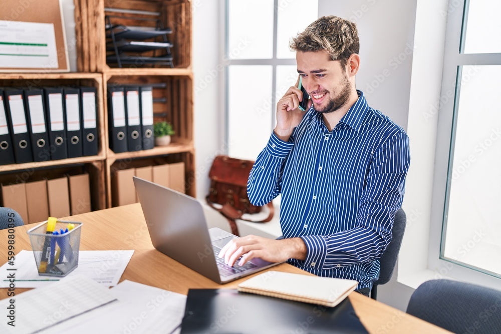 Young man business worker using laptop talking on smartphone at office Young man business worker using laptop talking on smartphone at office