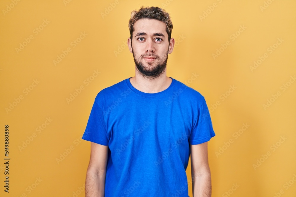 Hispanic man with beard standing over yellow background relaxed with serious expression on face. simple and natural looking at the camera. Hispanic man with beard standing over yellow background relaxed with serious expression on face. simple and natural looking at the camera.